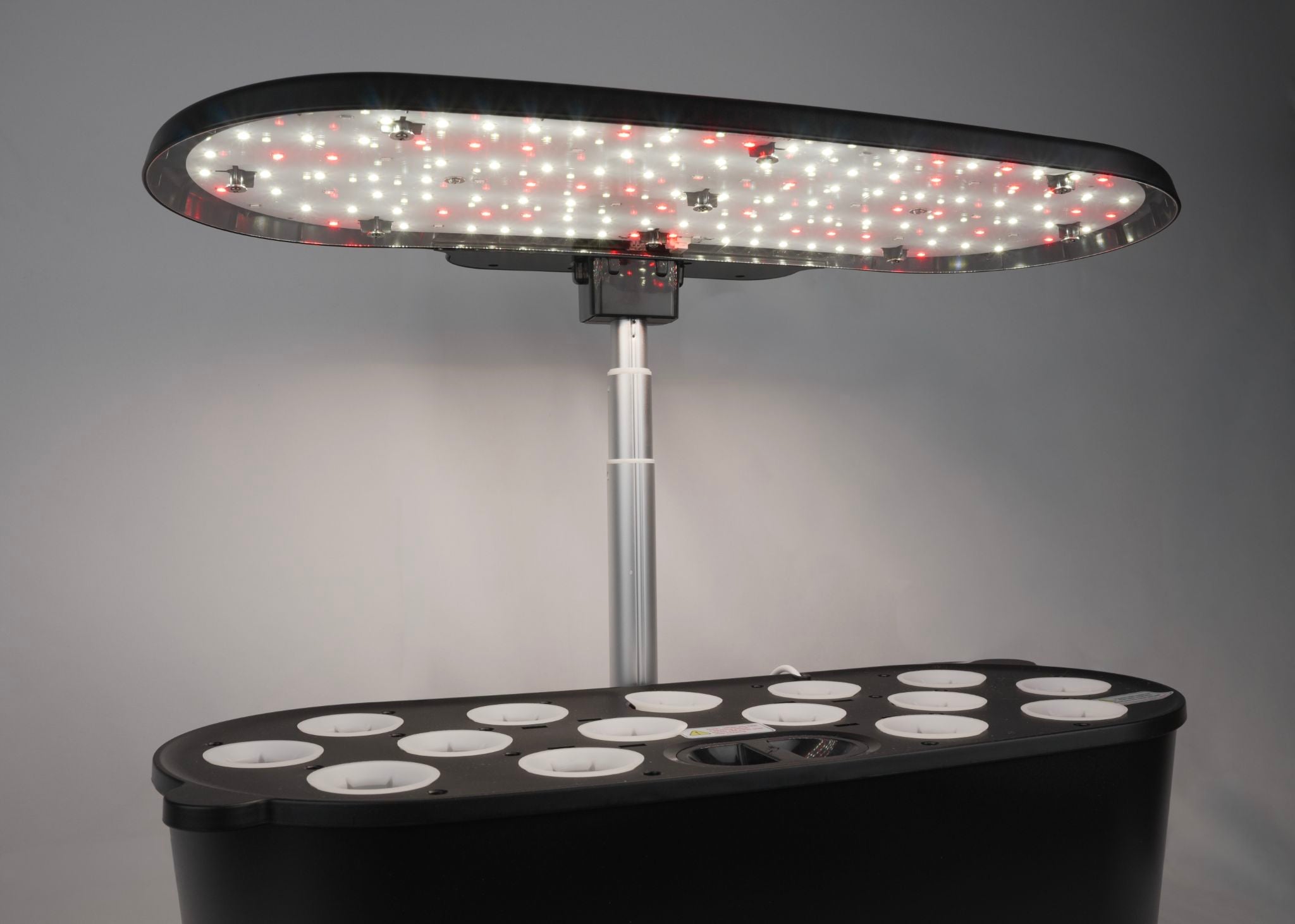 Black indoor smart garden (empty) with a warm-toned LED grow light on and set to fruit and flowering mode.
